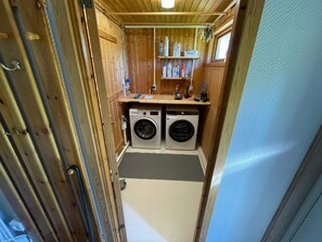 A compact laundry room with two front-loading washing machines, a shelf with cleaning supplies, and a wooden interior. - 4 Star Holiday Home in Onsala (Gottskar)