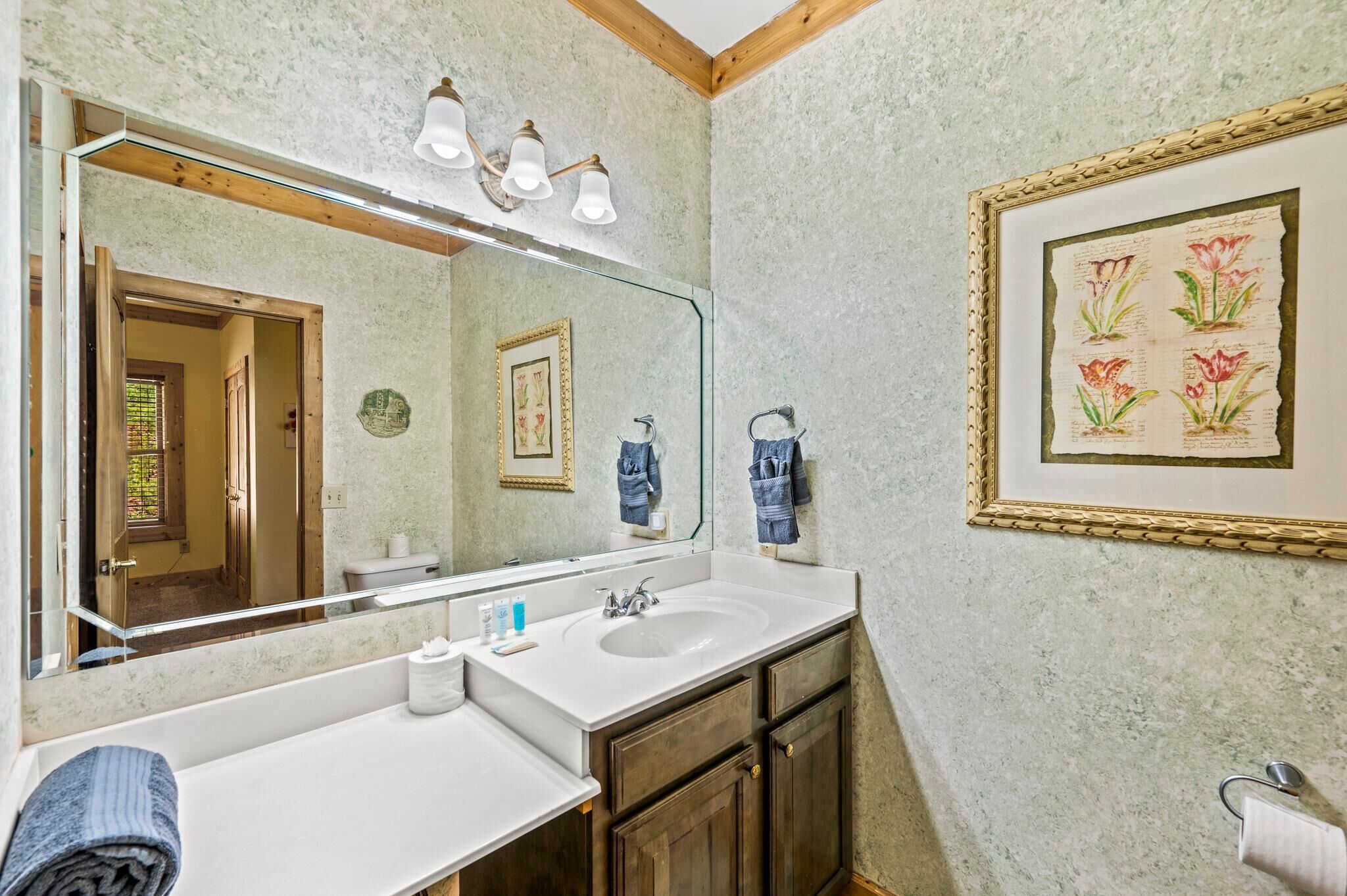 A bathroom with a large mirror, two sinks, wooden cabinets, and a framed botanical print on the wall.