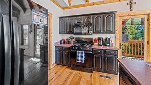 A modern kitchen with dark cabinetry, a stainless steel refrigerator, a stove, and a microwave. - Snail's Pace (Sevierville)