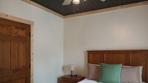 Quarto com porta de madeira, mesa de cabeceira, cama com encosto e relógio de parede.