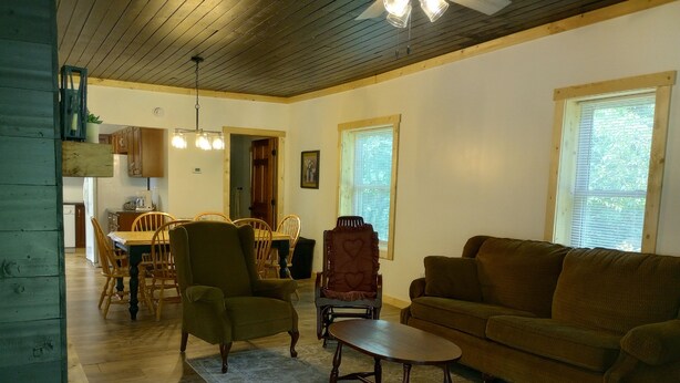 Uma sala de estar com sofá, poltronas, mesa de centro e um espaço de jantar com mesa e cadeiras.