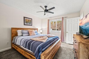 Een slaapkamer met een houten bed, een plafondventilator, een deur met uitzicht en een televisie op een houten dressoir.