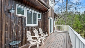A wooden deck with Adirondack chairs and a small table, overlooking a forested area. - Smoky Dreams 2 (Gatlinburg)