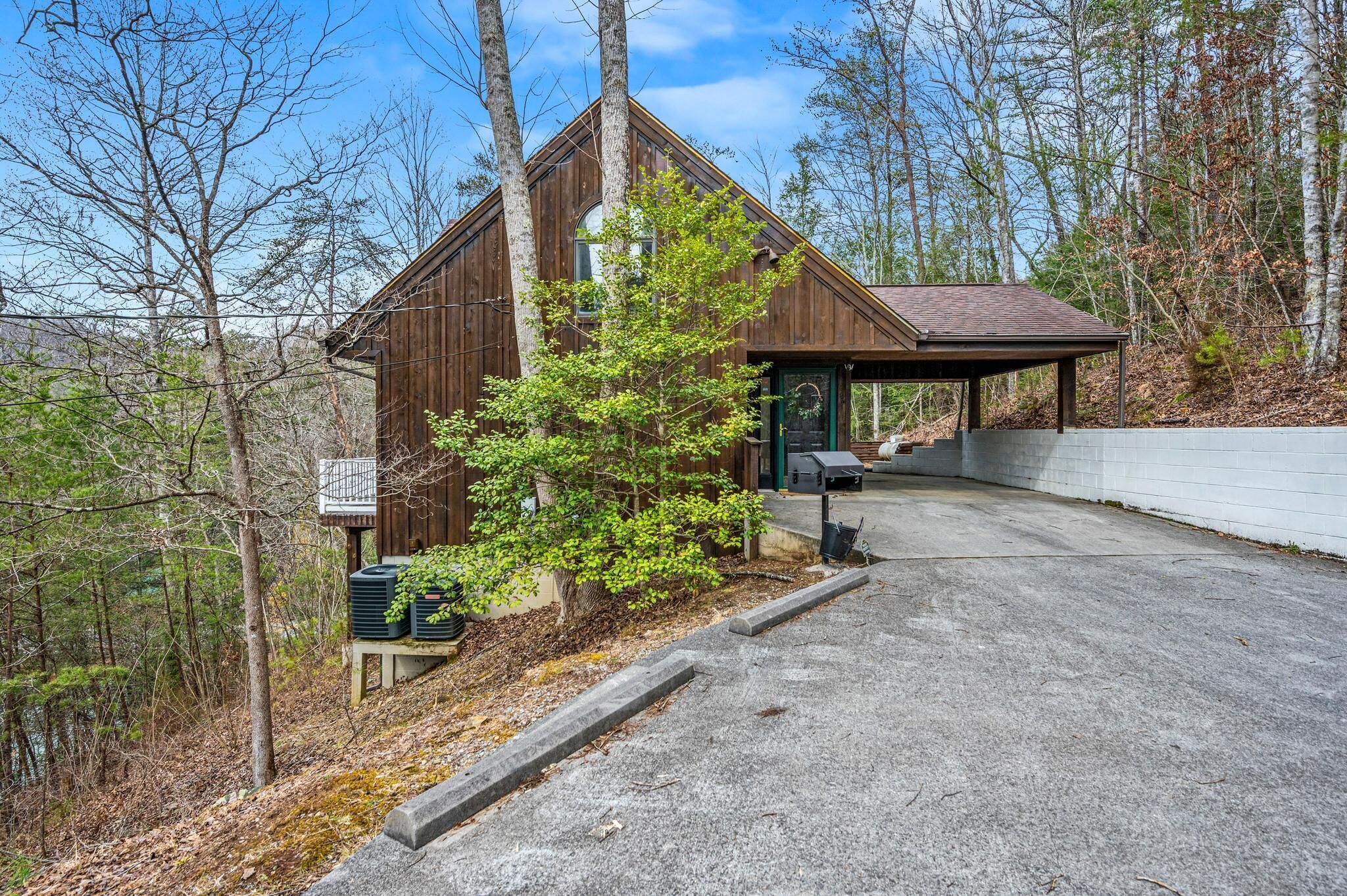 A rustic wooden cabin with a covered porch, surrounded by trees and a clear sky.