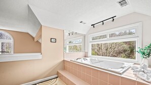 A modern bathroom with a large bathtub, a window with a view of trees, and a built-in bench. - Smoky Dreams 2 (Gatlinburg)
