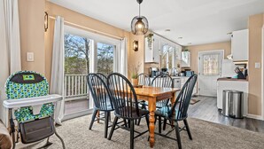 A dining area with a wooden table and chairs, a high chair, a hanging light fixture, and a view through large windows. - Smoky Dreams 2 (Gatlinburg)