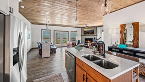 A spacious kitchen with wooden ceiling, a central island with a sink, and a dining area with a fireplace. - Premier Mountain Views (Gatlinburg)