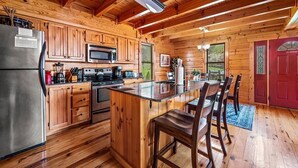 Interior de una cabaña de madera con cocina, comedor y una puerta roja.