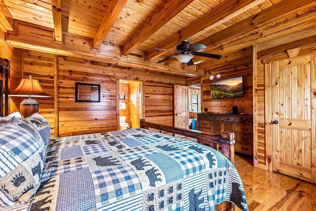 A log cabin bedroom with a bed, a ceiling fan, a TV, and a wooden door.