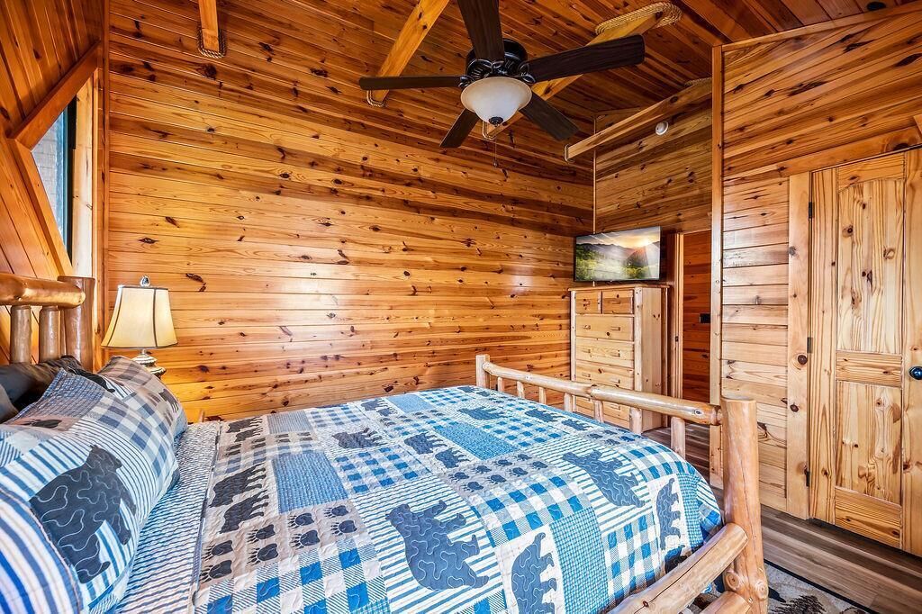 Ein Blockhauszimmer mit einem Bett, einem Deckenventilator, Holzwänden, einem Fernseher und einem Kleiderschrank.