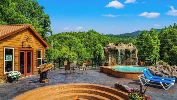 Una cabaña de madera con puerta roja, jacuzzi, cascada y mobiliario exterior.