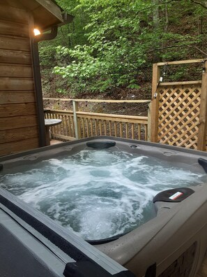 A hot tub with a wooden deck and a wooden fence in a wooded area. - Sleepy Bear (Sevierville)