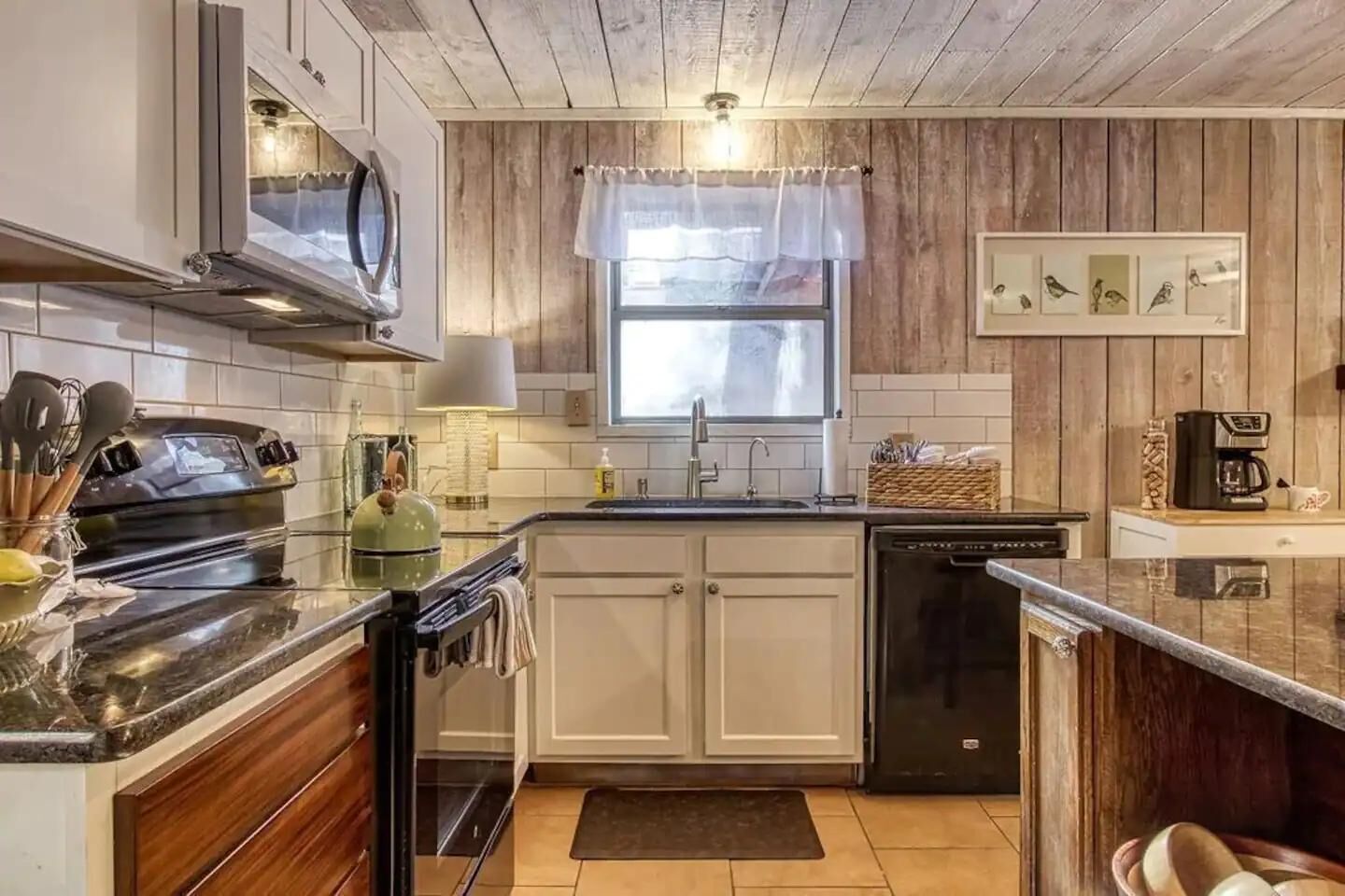 A kitchen with a stove, oven, dishwasher, and a window with a curtain.