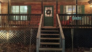 A wooden cabin with a green door, a staircase leading to the entrance, and a sign reading 'Sleepy Bear 3229 Bear Mountain Lane.' - Sleepy Bear (Sevierville)