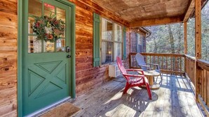 A wooden cabin with a green door, a porch with two Adirondack chairs, and a view of trees. - Sleepy Bear (Sevierville)