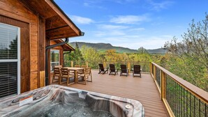 Una terraza de madera con hidromasaje, mobiliario exterior y vistas a montañas.