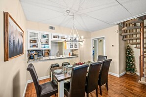 A dining area with a wooden table and chairs, a kitchen with white cabinets, and a staircase with a cat tree. - My Happy Place (Gatlinburg)