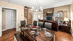 Comedor con una mesa de madera dispuesta para cuatro, una araña y una escalera que sube a otro nivel.