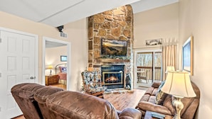 Una sala de estar con chimenea de piedra, sofás de cuero y televisor.
