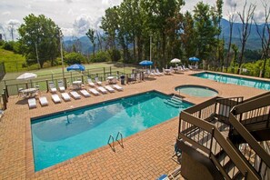 A swimming pool with lounge chairs and umbrellas, surrounded by trees and mountains. - My Happy Place (Gatlinburg)