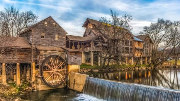 Un molino de agua rústico con edificios de madera y una gran rueda hidráulica.
