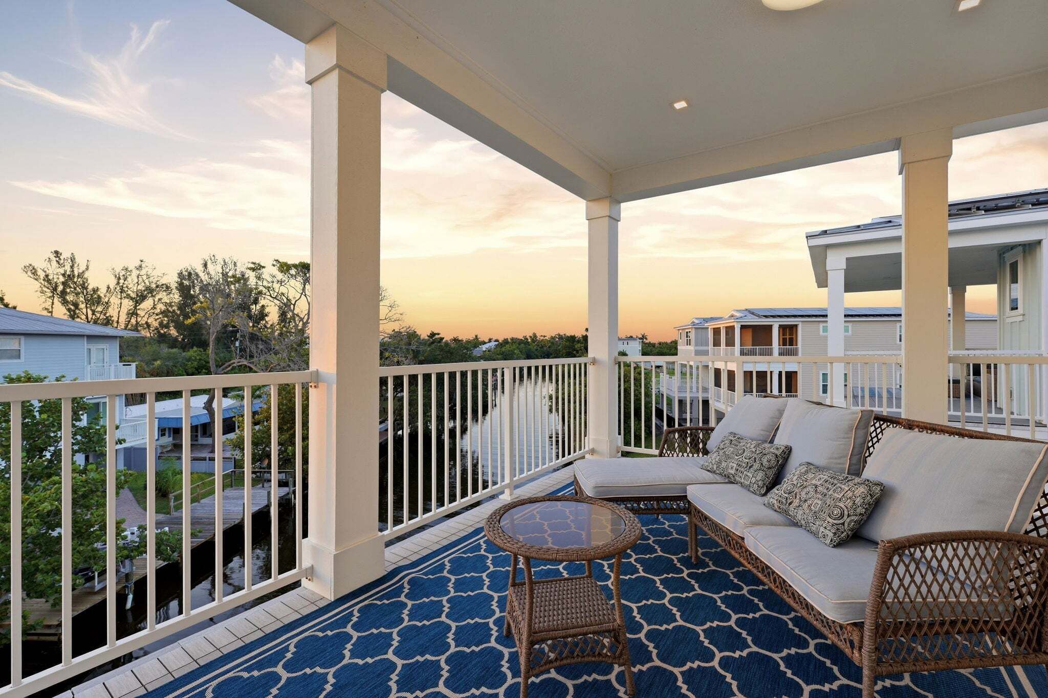 A covered balcony with a sofa, wicker chairs, and a glass table.