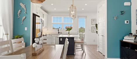 A modern kitchen with white cabinets, a wooden dining table, and a hanging light fixture.