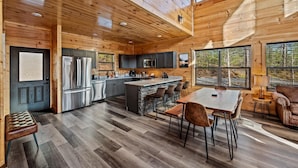 Ein modernes Interieur einer Blockhütte mit Küche, Essbereich und großen Fenstern.