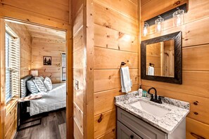 A wooden cabin interior with a bed, a bathroom with a sink, and a mirror. - Calling Mountains (Sevierville)