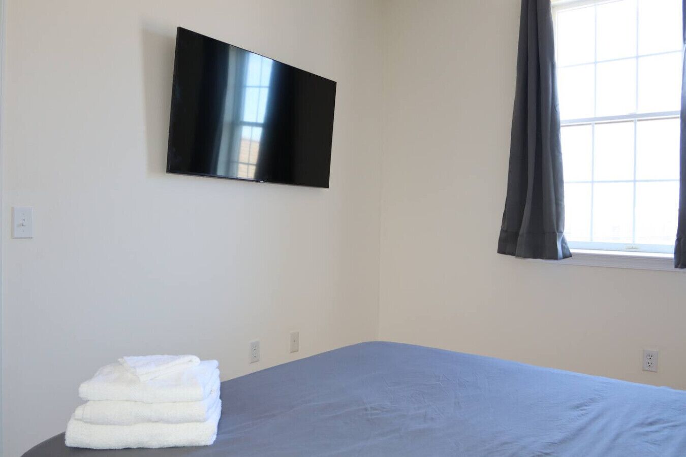 Un dormitorio con cama, televisor de pantalla plana en la pared y ventana con cortinas.
