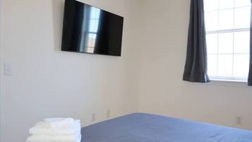 Un dormitorio con cama, televisor de pantalla plana en la pared y ventana con cortinas.