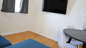 A room with a flat-screen TV mounted on the wall, a dining table with chairs, and a blue sofa.