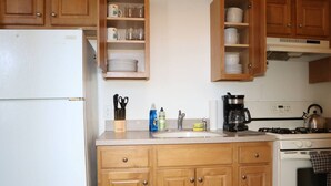 A kitchen with wooden cabinets, a white refrigerator, a sink, a stove, and various kitchen utensils.