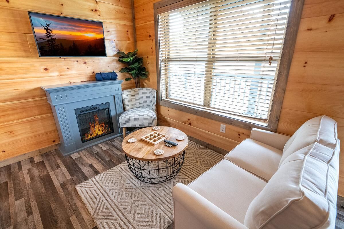 Ein gemütliches Blockhauss-Interieur mit Kamin, einer Couch, einem runden Couchtisch und einem an der Wand befestigten Fernseher.