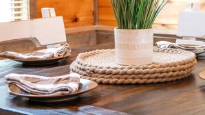 Interior de madera con una mesa lista para comer, que incluye un mantel individual tejido y una planta en maceta.