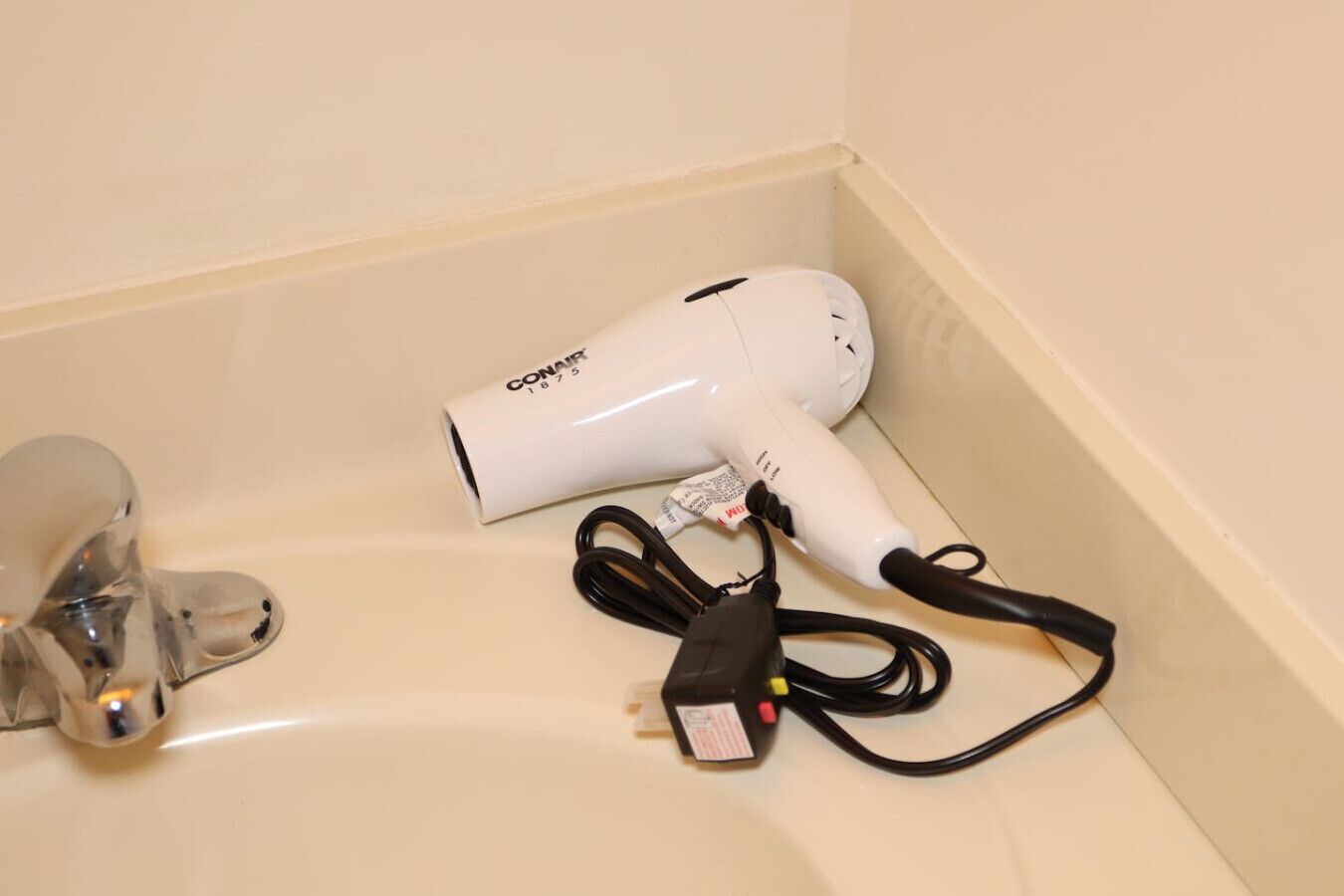 A white hair dryer with a cord and a plug on a beige countertop.