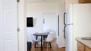 Un passadís amb zona de menjador que disposa d'una taula rodona i cadires, un refrigerador i armaris de fusta.