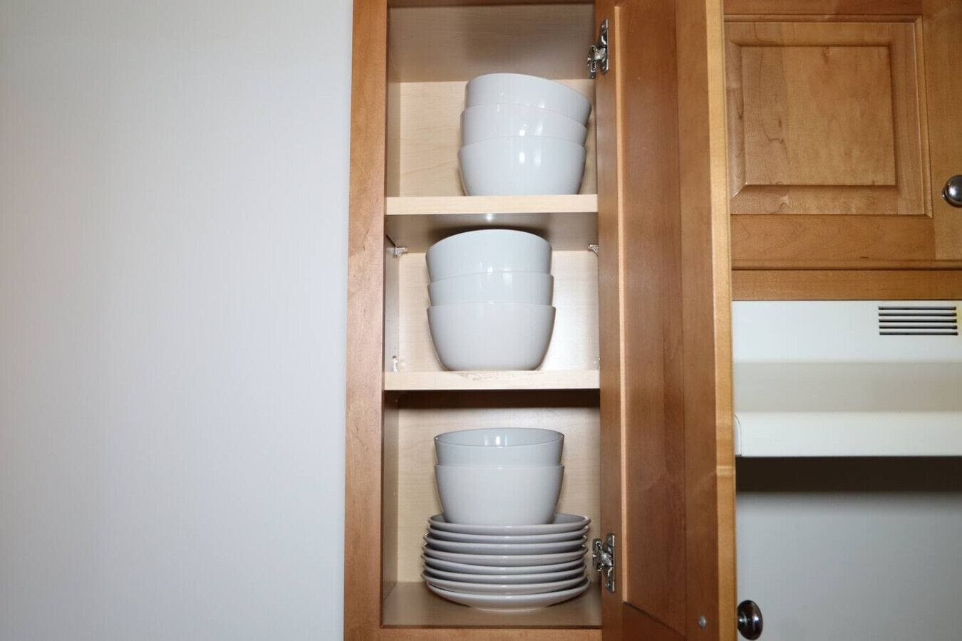 Een houten kast met drie planken, elk gevuld met witte kommen en borden.