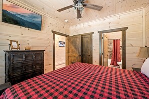 A bedroom with a bed, a dresser, a ceiling fan, and a painting on the wall. - Cabin By The Creek (Sevierville)