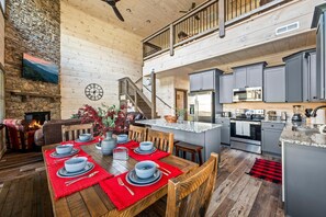 A spacious dining area with a high ceiling, a fireplace, and a kitchen with modern appliances. - Cabin By The Creek (Sevierville)