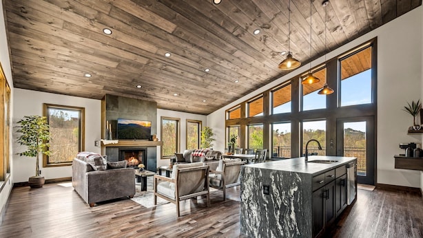 A spacious living area with a fireplace, large windows, and a kitchen island. - Majestic Overlook (Sevierville)