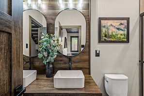 Ein Badezimmer mit Holzwandverkleidung, einem weißen Waschbecken, einer rechteckigen Spüle, einer Toilette und einem gerahmten Landschaftsbild.