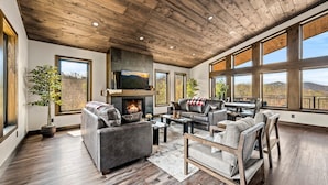 A spacious living room with a fireplace, leather sofas, and large windows offering a view of the outdoors. - Majestic Overlook (Sevierville)