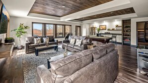 A spacious living room with a large sectional sofa, a coffee table, and a dining area with a kitchen in the background. - Majestic Overlook (Sevierville)