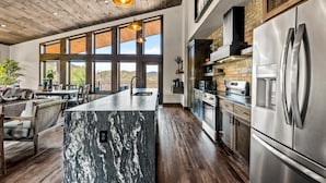 A modern kitchen with a large island, stainless steel appliances, and a wooden ceiling. - Majestic Overlook (Sevierville)