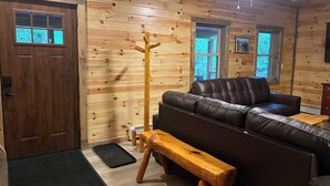 A log cabin interior with a leather sofa, wooden bench, and a coat rack.
