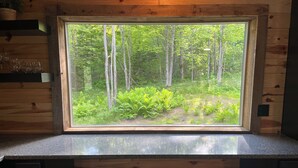 A wooden cabin interior with a large window overlooking a forest.