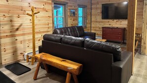 A log cabin interior with a leather sofa, wooden bench, and a TV mounted on the wall.