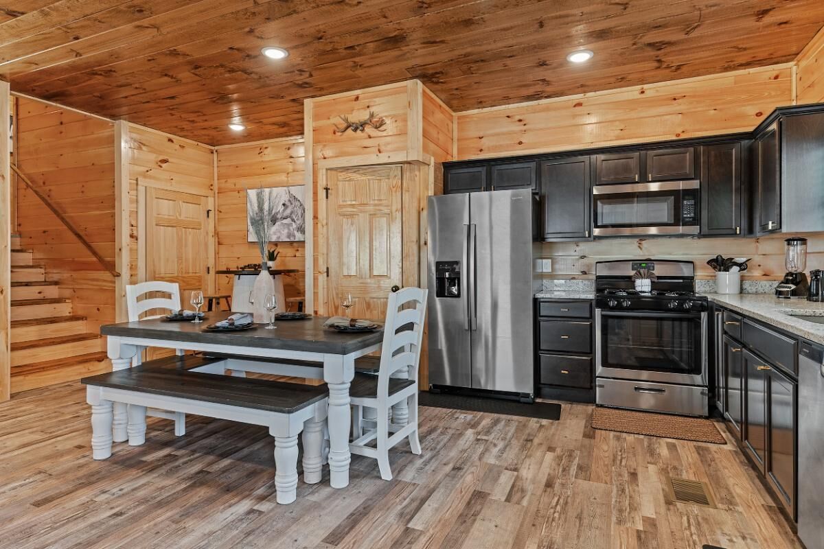 A wooden interior with a dining table, chairs, a refrigerator, a stove, and a microwave.