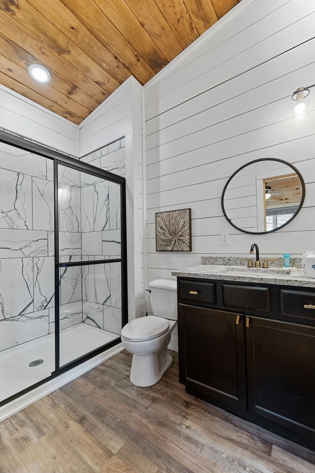 A modern bathroom with a glass shower enclosure, a toilet, a sink with a mirror, and wooden flooring.